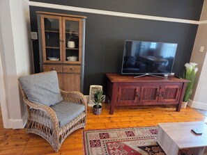 A living room with a wicker chair, a wooden cabinet, a television, and a patterned rug.