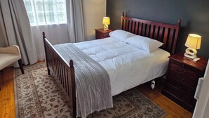 A bedroom with a wooden bed, two bedside lamps, a nightstand, a chair, and a window with curtains.