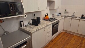 A compact kitchen with white cabinets, a stainless steel dishwasher, a built-in microwave, a gas stove, and a wooden floor.