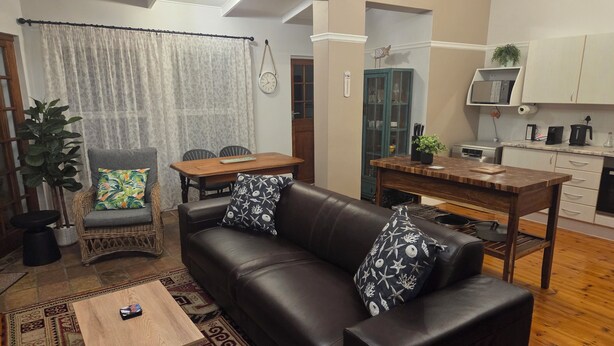 A living room with a leather sofa, a coffee table, a dining table, and a kitchen area with cabinets and appliances.