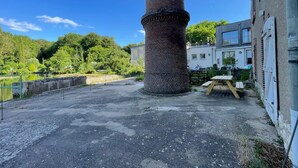 A brick chimney, a paved area, and a building with a balcony. - Newly built holiday cottage in a mill by the Loir River (Marboué)