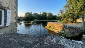 A canal with a water wheel, a stone building with a window, and trees in the background. - Newly built holiday cottage in a mill by the Loir River (Marboué)