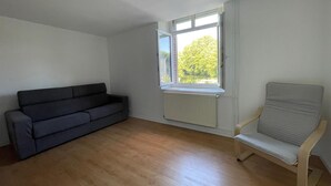 A room with a dark grey sofa, a light grey chair, and a window with a view of greenery. - Newly built holiday cottage in a mill by the Loir River (Marboué)