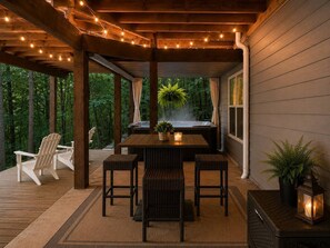 An outdoor patio with a wooden table and chairs, a hot tub, and string lights. - River Resort Retreat | Hot Tub & Game Room | Pets (Ellijay)