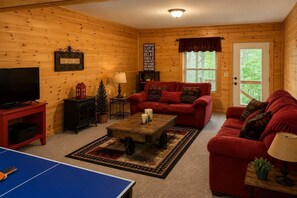 Interior acogedor de una cabaña con un sofá rojo, un televisor, una mesita y una mesa de ping pong.