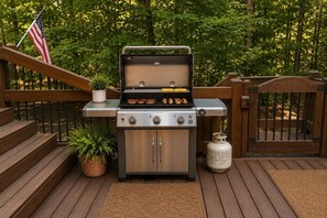 Ein Grill für den Außenbereich mit Gasflasche, einer Holzterrasse und einem Metallzaun.