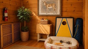 Una habitación acogedora con extintor, un cuadro de un ciervo enmarco, una planta, una cama para mascotas y un rompecabezas sobre una mesita.