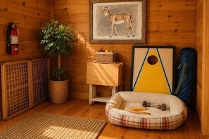 Ein gemütliches Zimmer mit Feuerlöscher, einem Bild von einem Reh, einer Pflanze, einem Haustierbett und einem Puzzle auf einem kleinen Tisch.