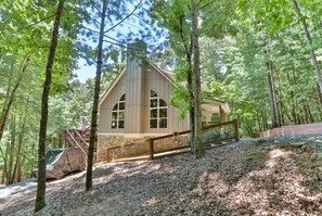 Uma cabana com uma escadaria íngreme, varanda coberta e vista para uma área arborizada.