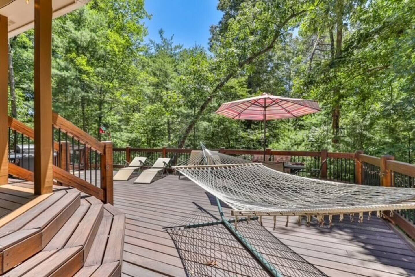 A wooden deck with a hammock, lounge chairs, and a red umbrella.