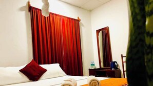 Ein Hotelzimmer mit einem Bett, einem Holznachttisch, einem Spiegel und einem roten Vorhang.