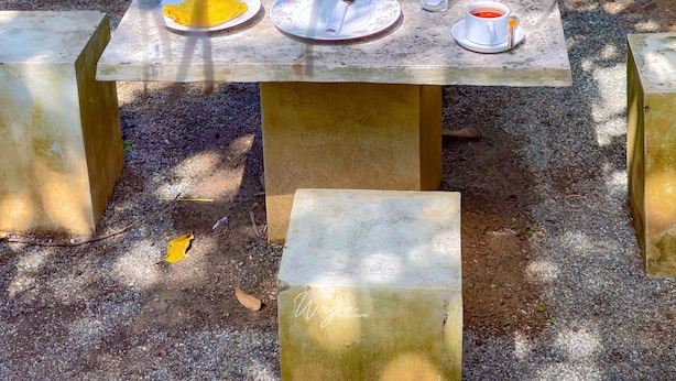 Ein Essplatz im Freien mit Speisen auf Tellern, einem Glas Saft und einer Tasse Tee.