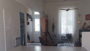 A dining area with a checkered floor, white chairs, a table with a polka dot tablecloth, and a window with a decorative curtain. - Fisherman's cottage on the Fouras Peninsula (Charente-Maritime) (Fouras)