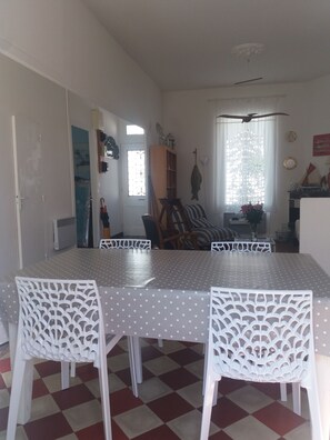 A dining area with a checkered floor, white chairs, a table with a polka dot tablecloth, and a window with a decorative curtain. - Fisherman's cottage on the Fouras Peninsula (Charente-Maritime) (Fouras)