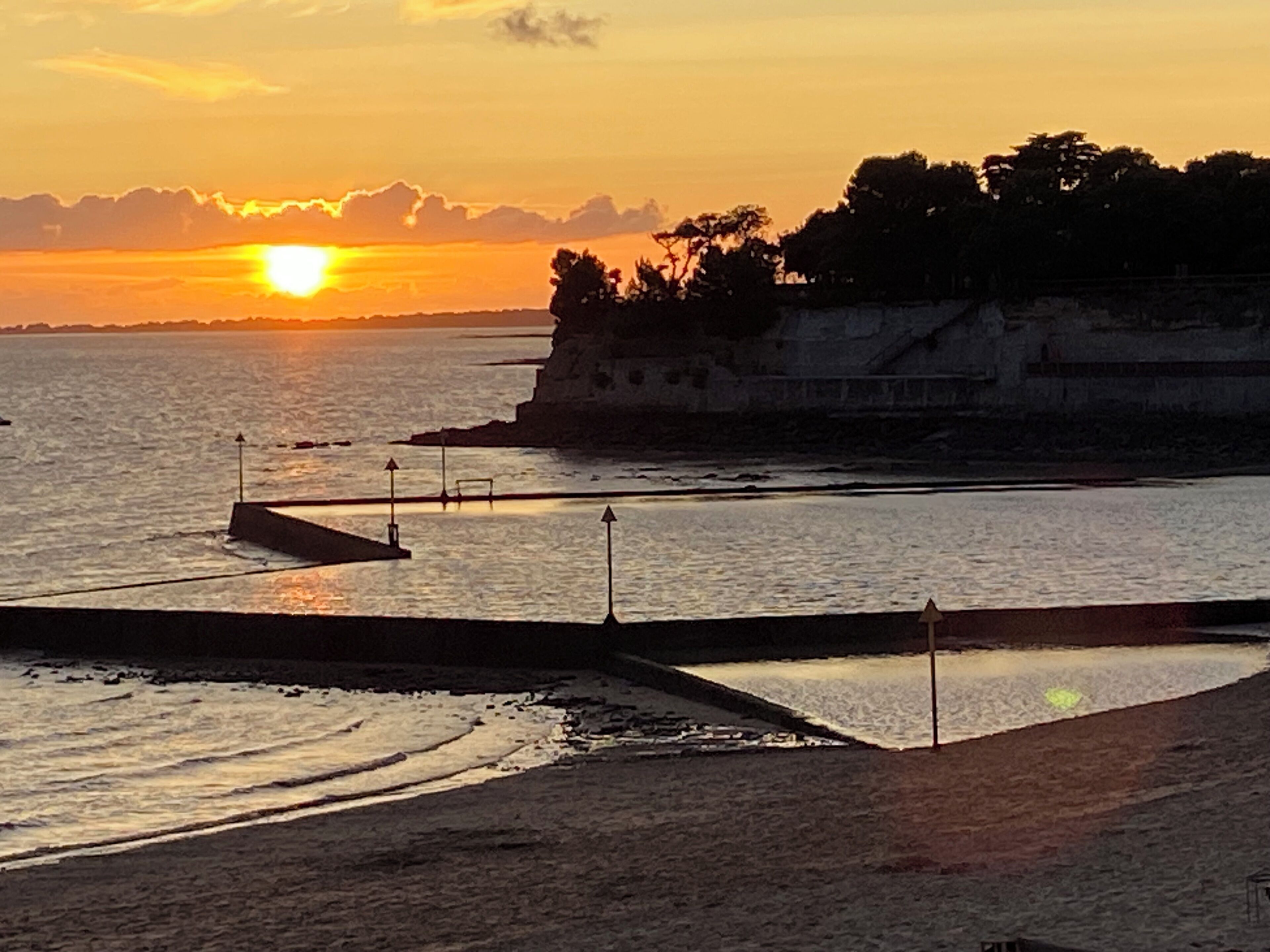 A coastal sunset view with a sandy beach, a rocky cliff, and calm sea.