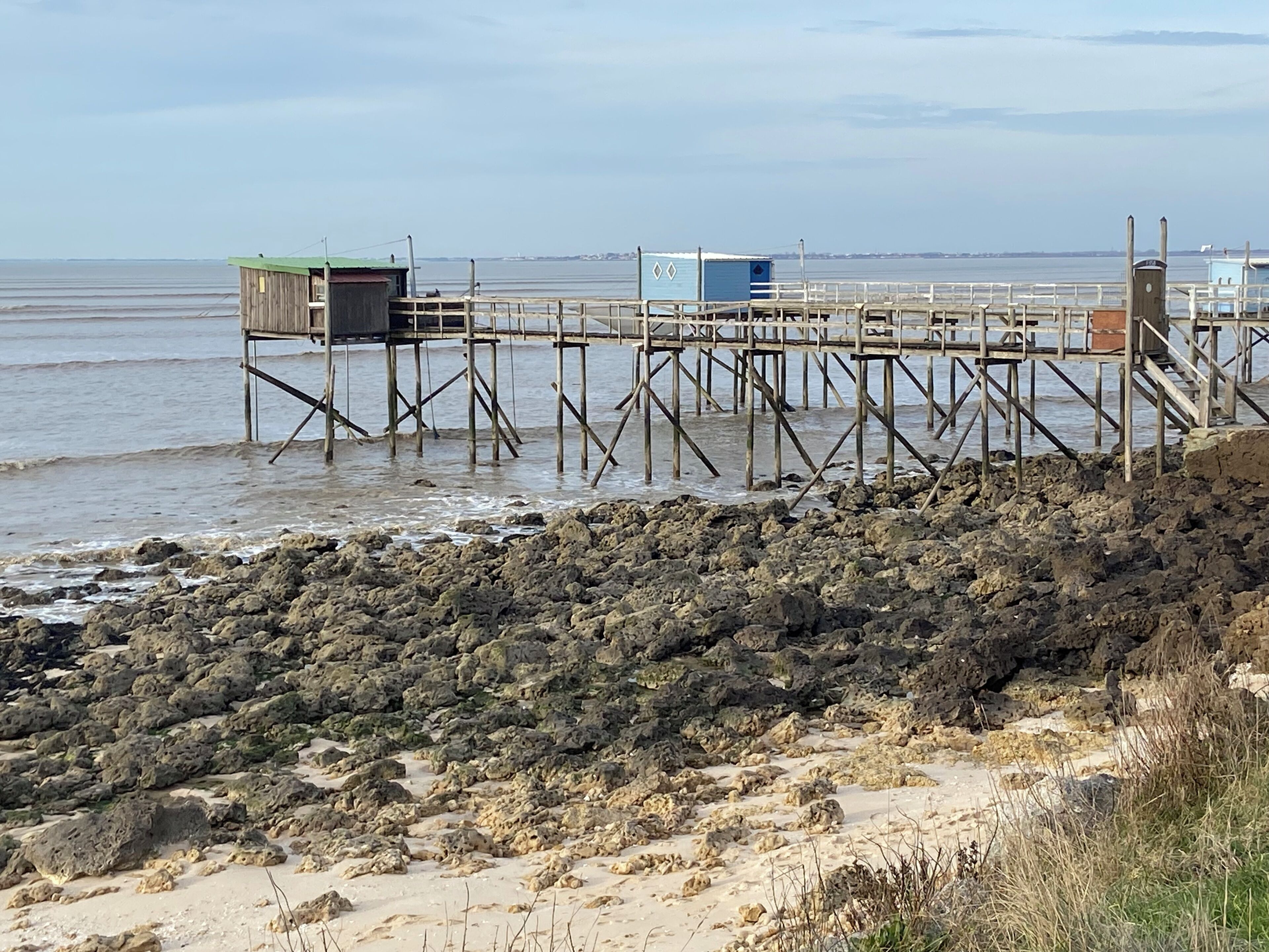 A pier with a wooden structure and a small building, extending into calm waters.