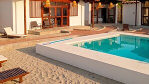Un complexe hôtelier doté d’une piscine, de chaises longues et d’un espace extérieur couvert avec des sièges.