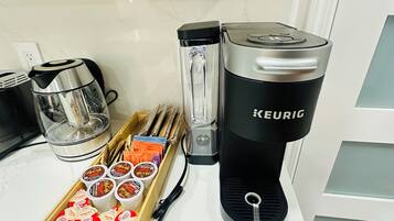 Un comptoir de cuisine avec une machine à café Keurig, une verseuse en verre, un plateau en bois contenant des dosettes McCafé et une bouilloire électrique noire.