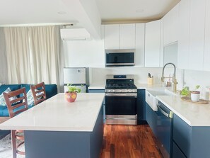 A modern kitchen with a central island, built-in appliances, and a dining area with blue chairs. - Luxury Multi-Level Suite with Deck & Mountain View (Renton)