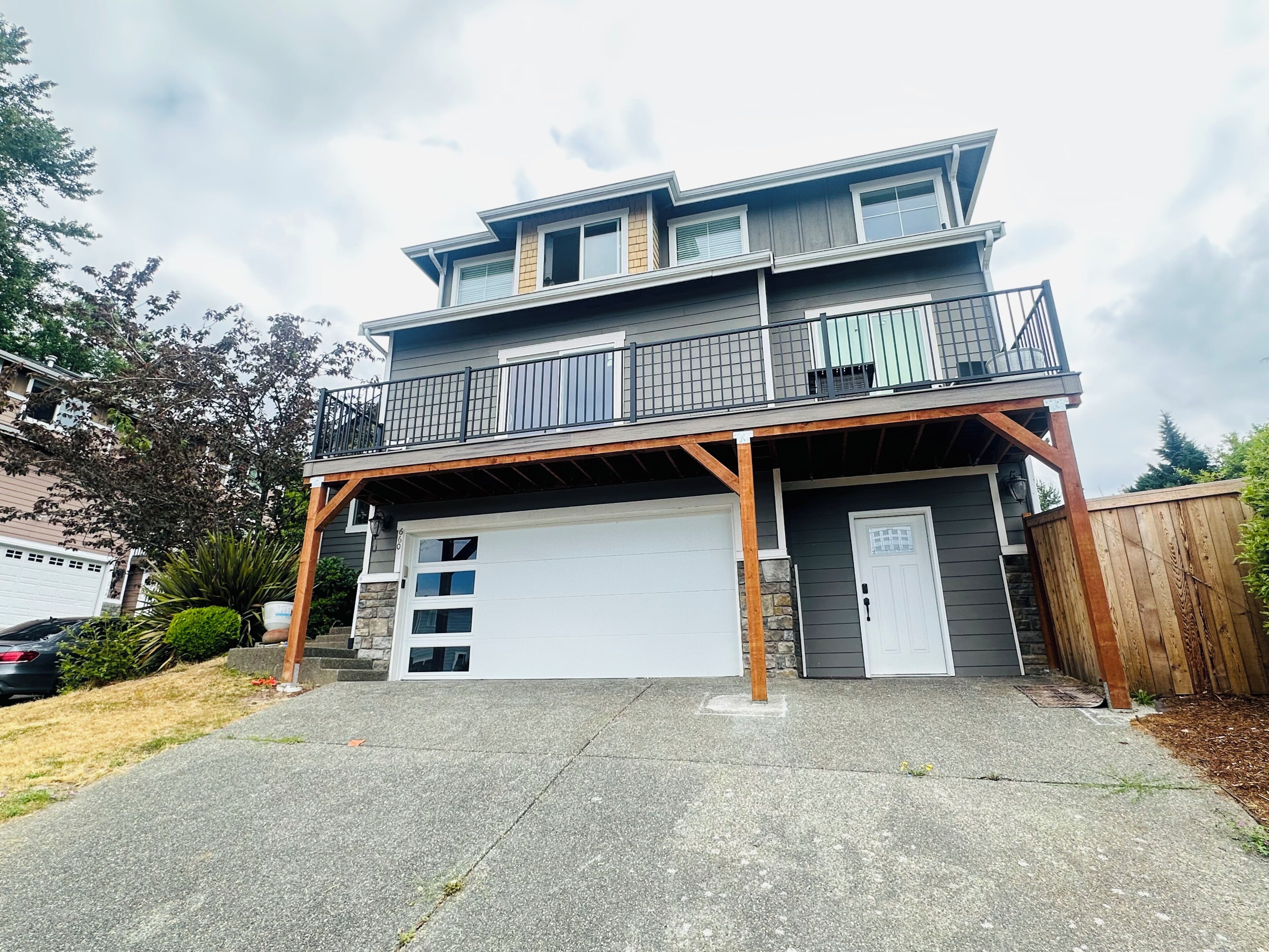 A two-story building with a garage, a balcony on the upper floor, and a wooden deck.