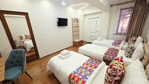 Een hotelkamer met twee bedden, een slaapbank, een stoel, een televisie en een deur.