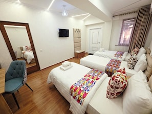 A hotel room with two beds, a sofa, a chair, a TV, and a door.