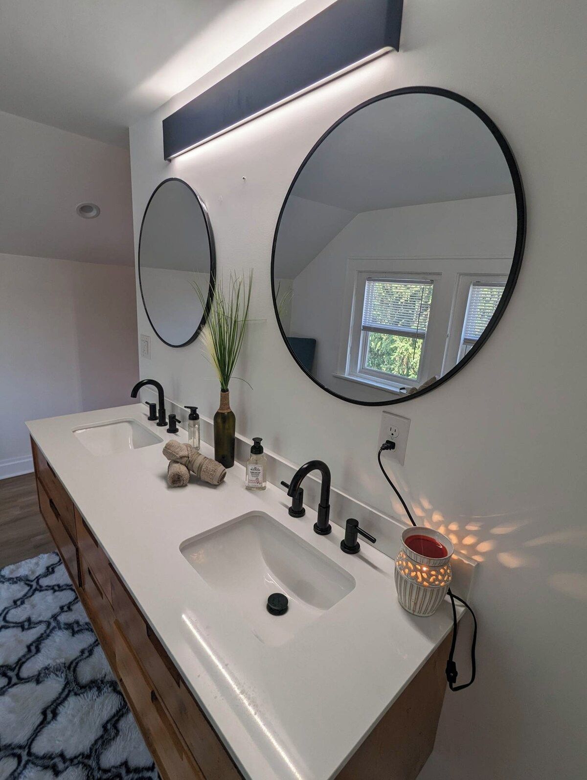 A bathroom with a double sink, two round mirrors, a plant, and a decorative candle holder.