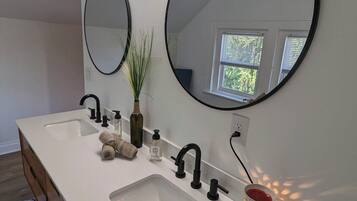 A bathroom with a double sink, two round mirrors, a plant, and a decorative candle holder.