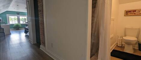 A hallway with a white door leading to a bathroom with a toilet and shower curtain.