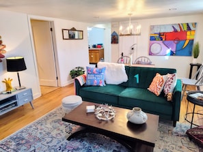 A living room with a green sofa, a coffee table, a lamp, and a painting on the wall. - Vintage garden level apt in fabulous,  quiet tree lined SugarHouse neighborhood (Salt Lake City)
