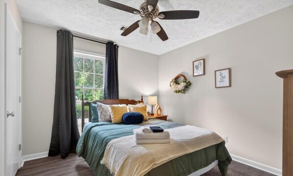 A bedroom with a bed, a ceiling fan, a window with curtains, and wall decorations.