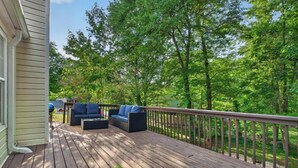 Eine Holzterrasse mit Gartenmöbeln, einer Brüstung und Blick auf ein bewaldetes Gebiet.