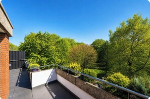 Un balcon doté d’une rambarde en métal, donnant sur un jardin aménagé et des arbres.