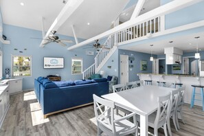Ein modernes Wohnzimmer mit einem blauen Sofa, einem Esstisch mit Stühlen, einer Küchenzeile und einer Treppe.
