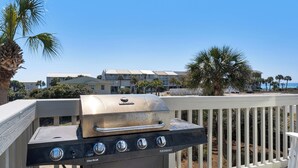 Una parrilla Char-Broil en un balcón con vista a un hotel frente a la playa y palmeras.