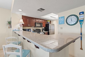 A kitchen with a central island, wooden cabinets, a microwave, and a refrigerator. - 🌴Edgewater #1400 | BeachFront 2BR condo | Pool 🏖️ (Miramar Beach)