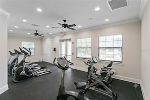 Ein Fitnessraum mit mehreren Trainingsgeräten, Deckenventilatoren und großen Fenstern.