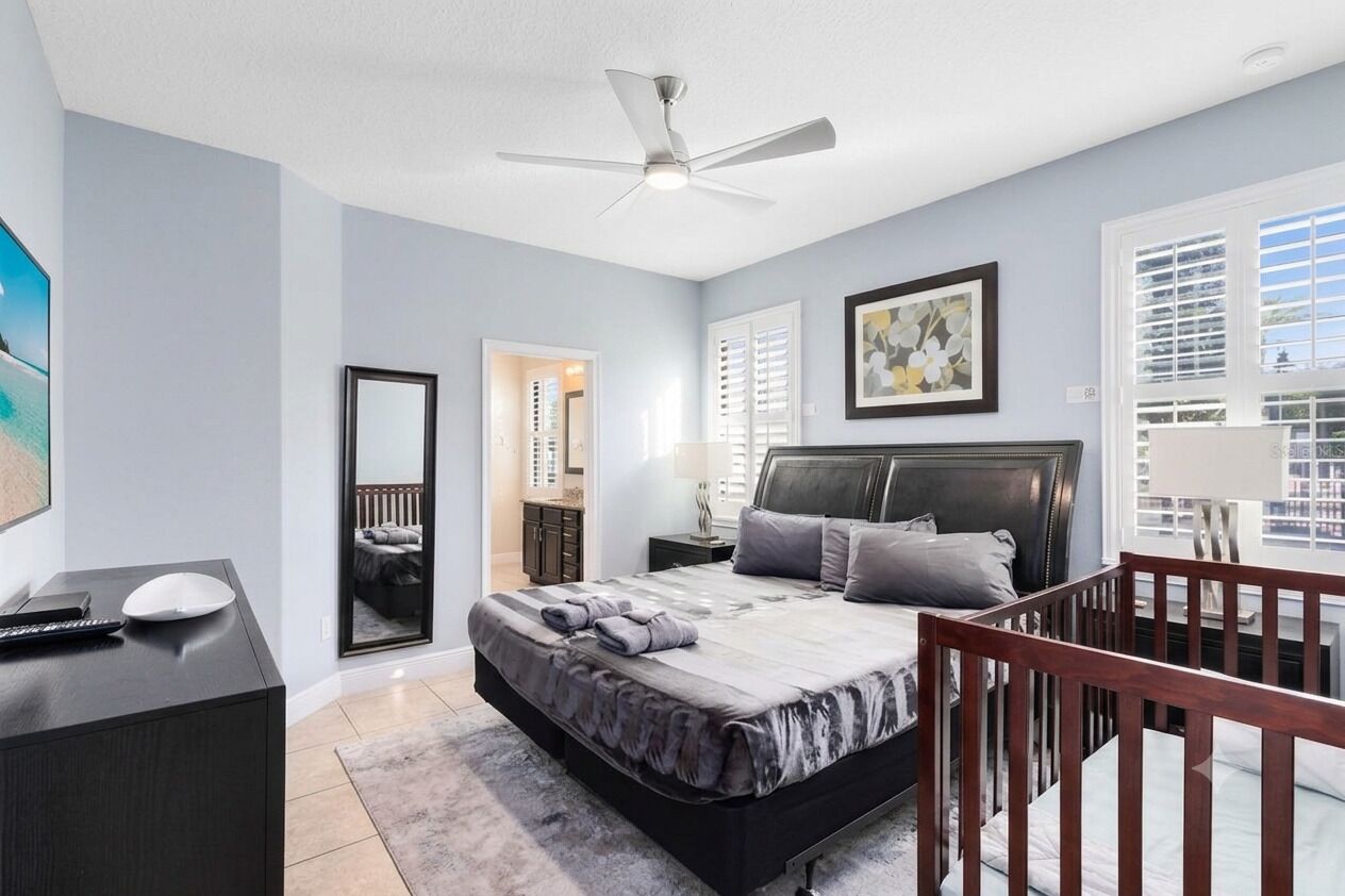 A bedroom with a bed, a desk, a chair, a ceiling fan, and a window with blinds.