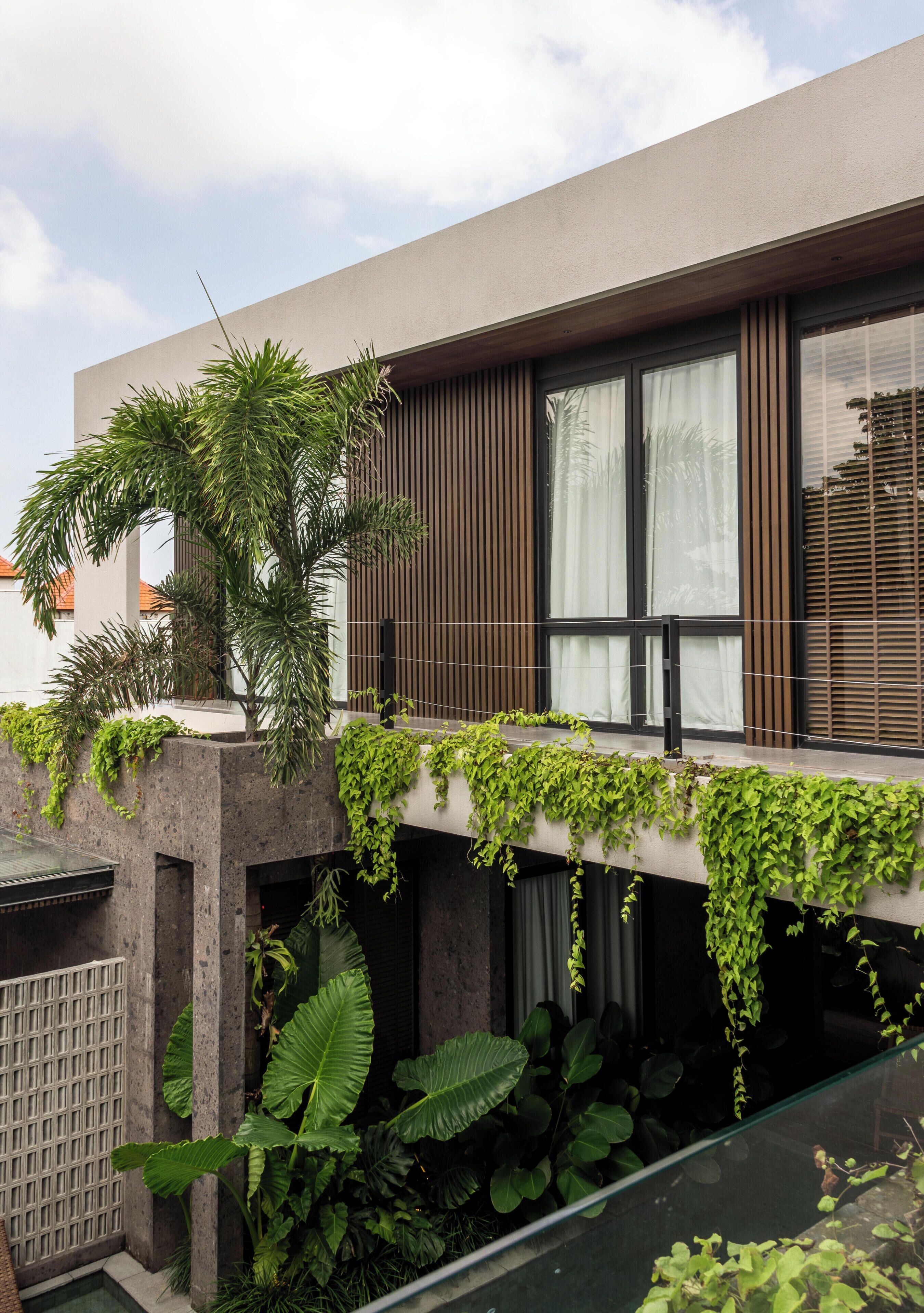 A modern building with a flat roof, large windows, and a balcony with greenery.