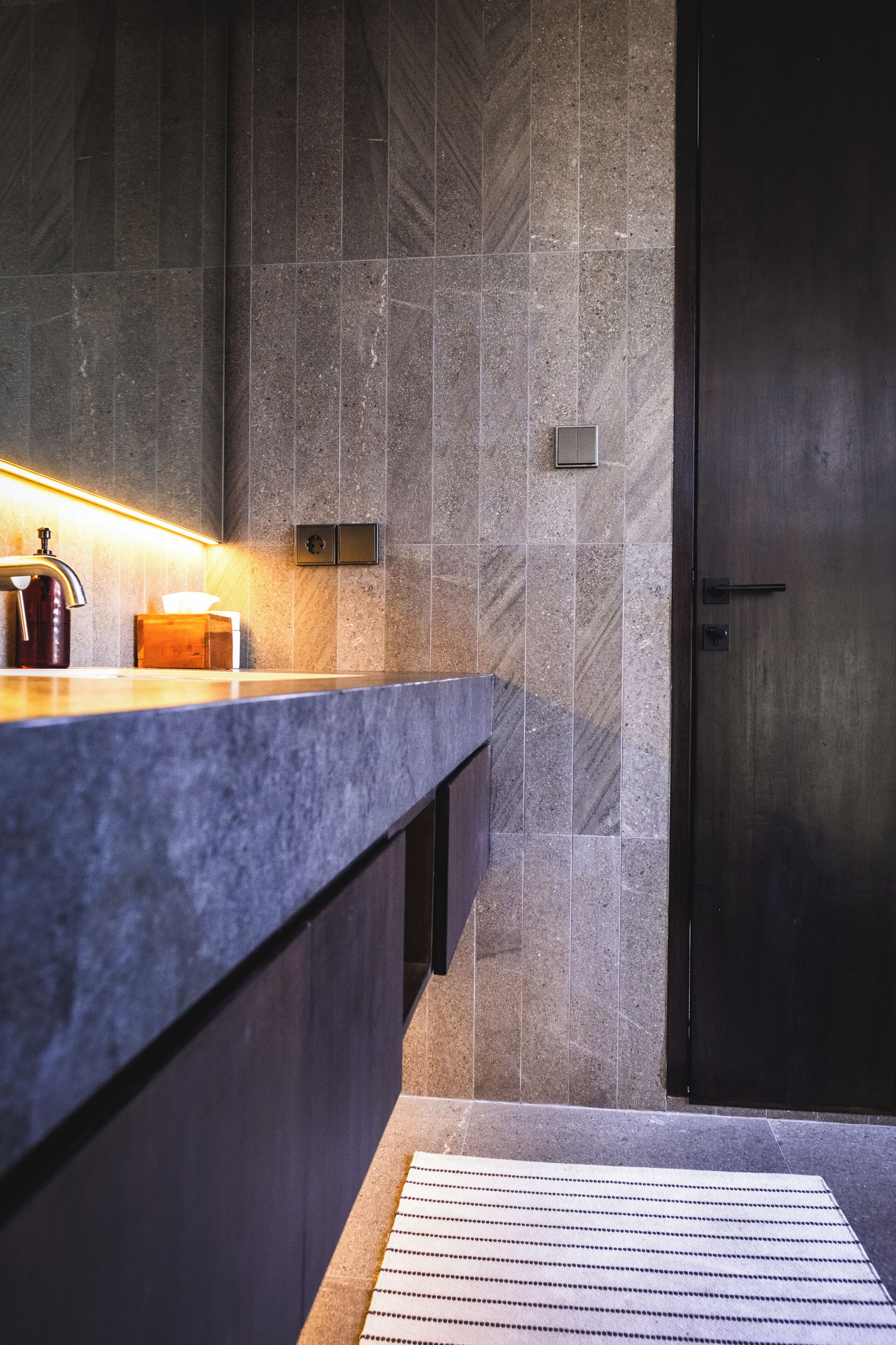A modern bathroom with a marble countertop, a hand soap dispenser, and a towel dispenser.