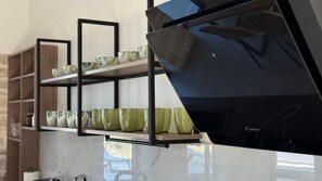 A kitchen with a black countertop, a shelf with decorative items, and a cabinet with glassware. - Sunrise Village Aptera Private Pool Villa II (Chania)