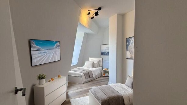 Ein modernes Schlafzimmer mit schrägem Dach, einem Bett, einer Kommode und einem Fenster.