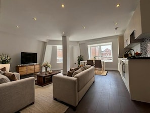 A modern living room with a sofa set, a coffee table, and a television. There is a dining area with a table and chairs, and a kitchen with cabinets and a countertop. - Boutique 2 bed apartment in Old Town, swindon (Swindon)