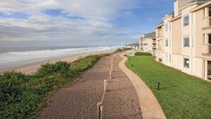 Uma área residencial costeira com um calçadão pavimentado que leva a uma praia, ao lado de um conjunto de edifícios de apartamentos.