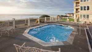 Uma piscina com vista para o oceano, rodeada por espreguiçadeiras e um edifício com varandas.