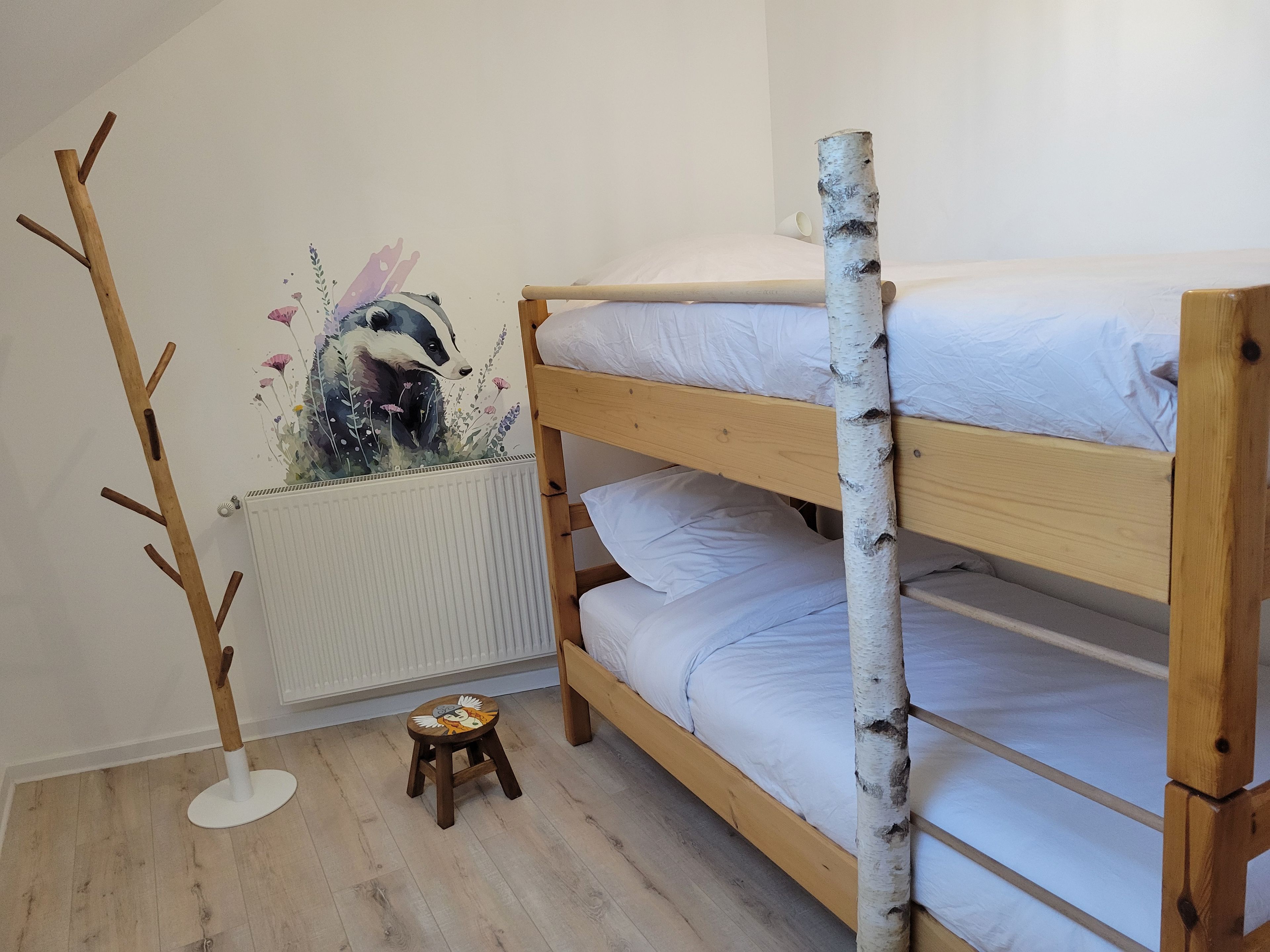 A bunk bed with a birch tree trunk decoration, a radiator, and a small stool with a bird design.