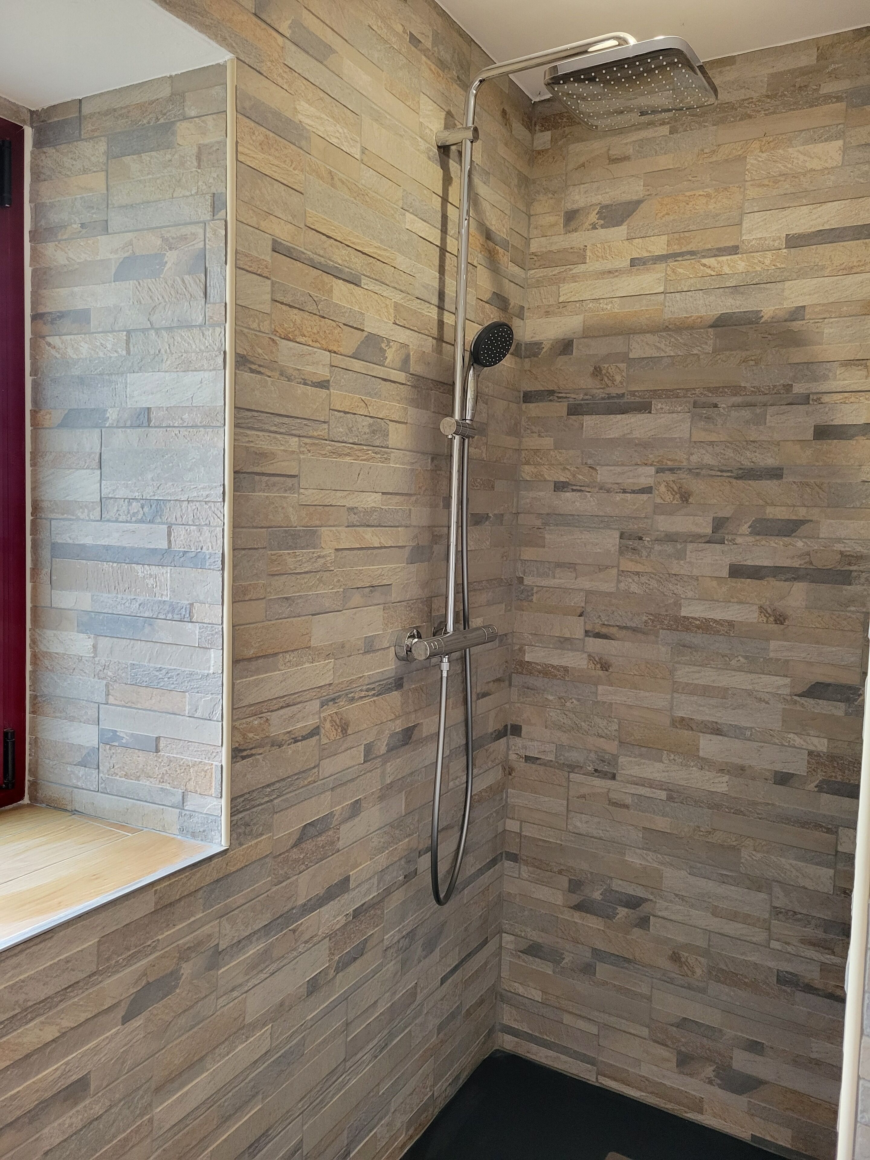 A shower with a rain showerhead and a handheld showerhead, set against a wall with a stone-like pattern.