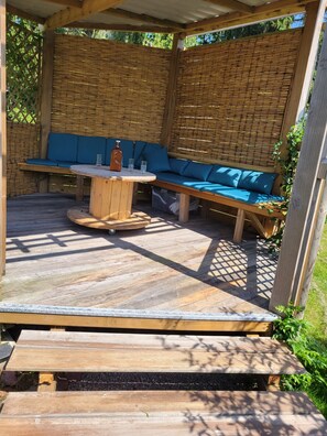 A wooden deck with a round table and blue cushioned seating. - A charming vacation rental on the outskirts of Brocéliande. (Iffendic)