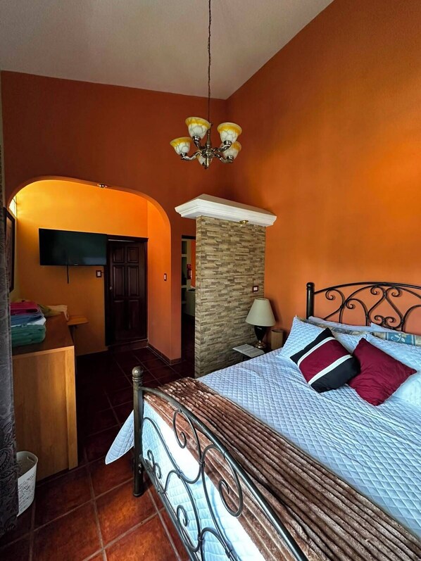 A bedroom with a bed, a desk, a television, and a stone pillar.