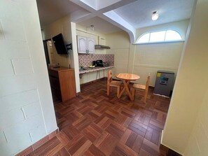 A compact kitchen with a herringbone floor pattern, a small dining table, and a built-in TV.